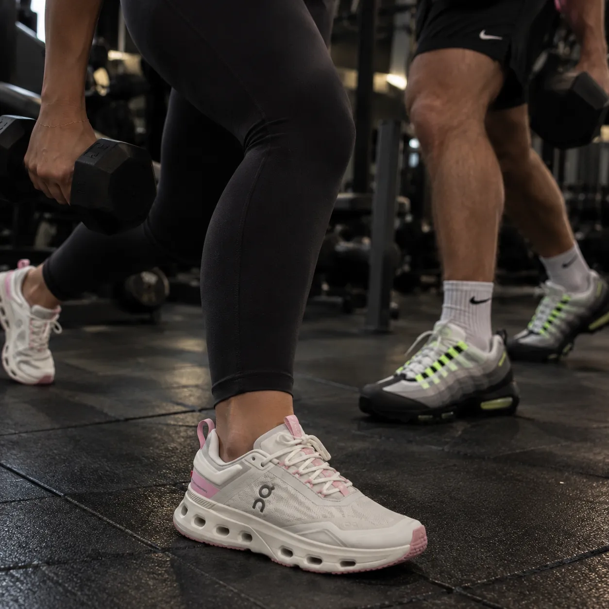 Personas entrenando con mancuernas en el gimnasio con tenis On y Nike