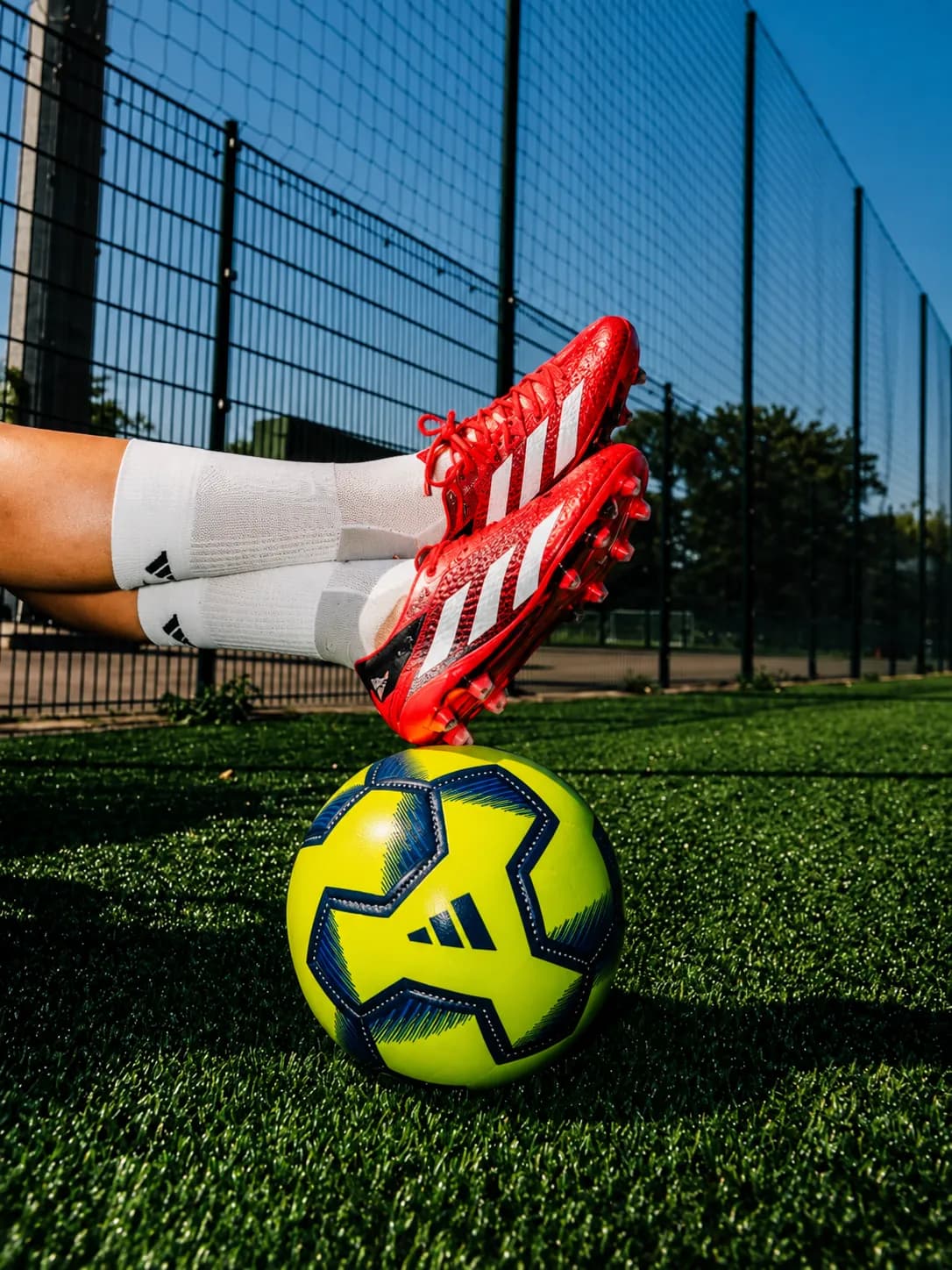 Tacos Adidas rojos sobre un balón en una cancha sintética